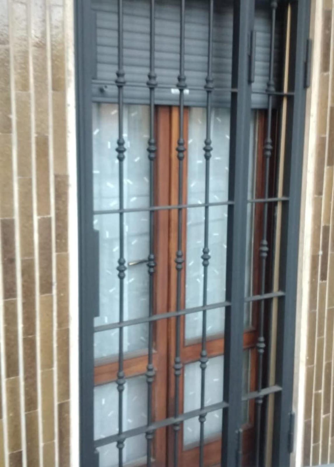 Finestra con grate di sicurezza decorative in ferro. La porta di legno è visibile dietro le grate.