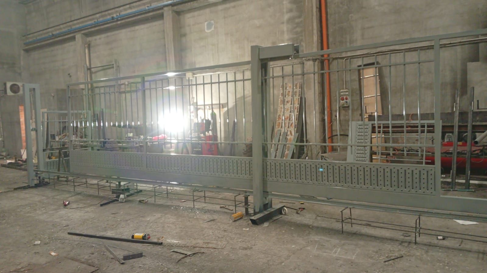 Cancello scorrevole in metallo grigio in costruzione in un'officina; il cancello è fissato su binari.