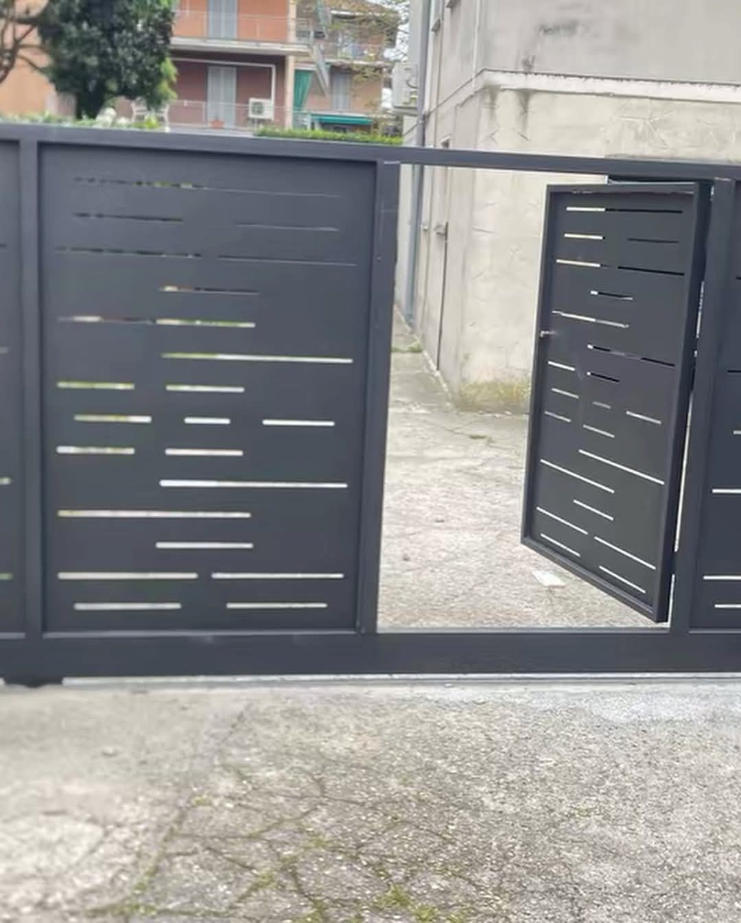 Cancello in metallo nero, parzialmente aperto, con ritagli orizzontali, su una superficie di cemento.