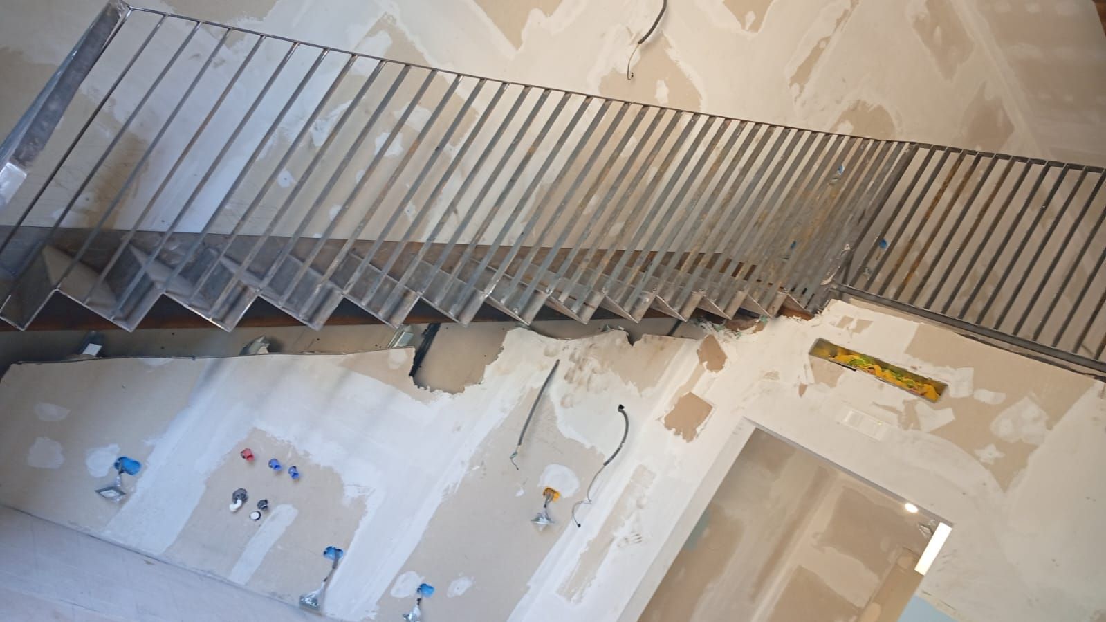 Scala con ringhiera in metallo in costruzione, contro pareti ruvide.