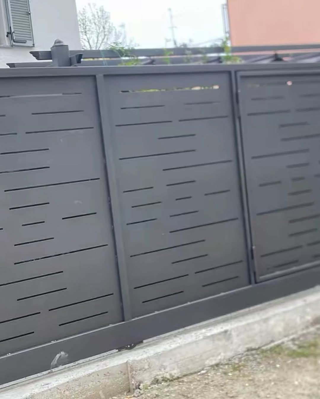 Cancello scorrevole in metallo grigio scuro con ritagli orizzontali e angolari.