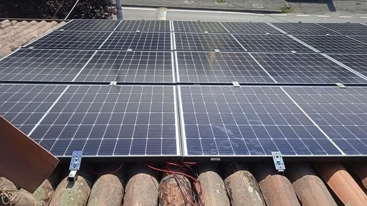 Pannelli solari installati su un tetto rivestito di tegole. Pannelli blu e neri. Staffe di montaggio visibili.