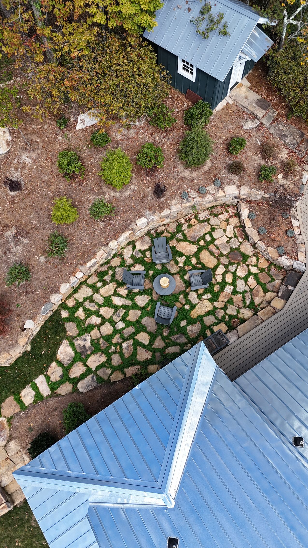 Man installing stone pavers in an outdoor kitchen area with a grill and counter, surrounded by trees.