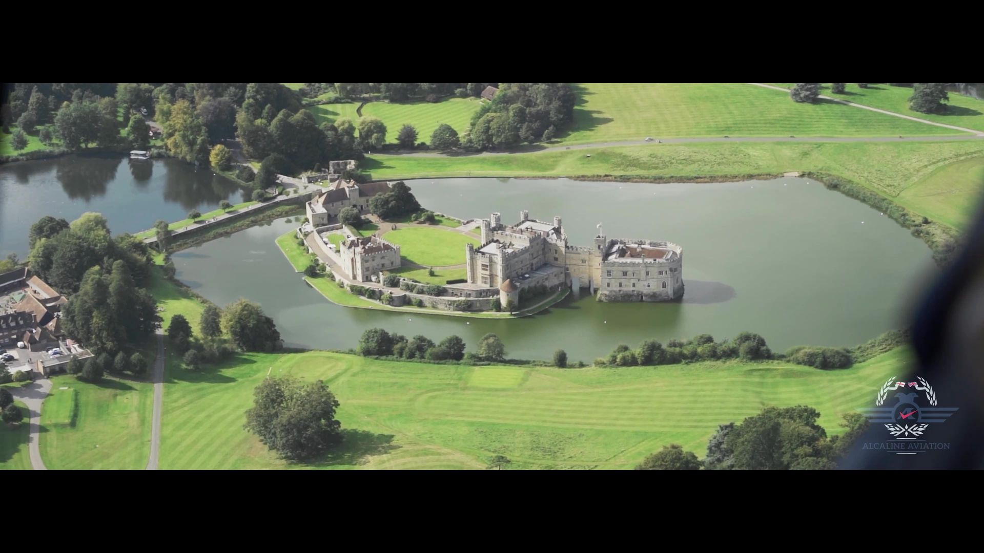 An aerial view of a castle on a small island in the middle of a lake surrounded by trees.