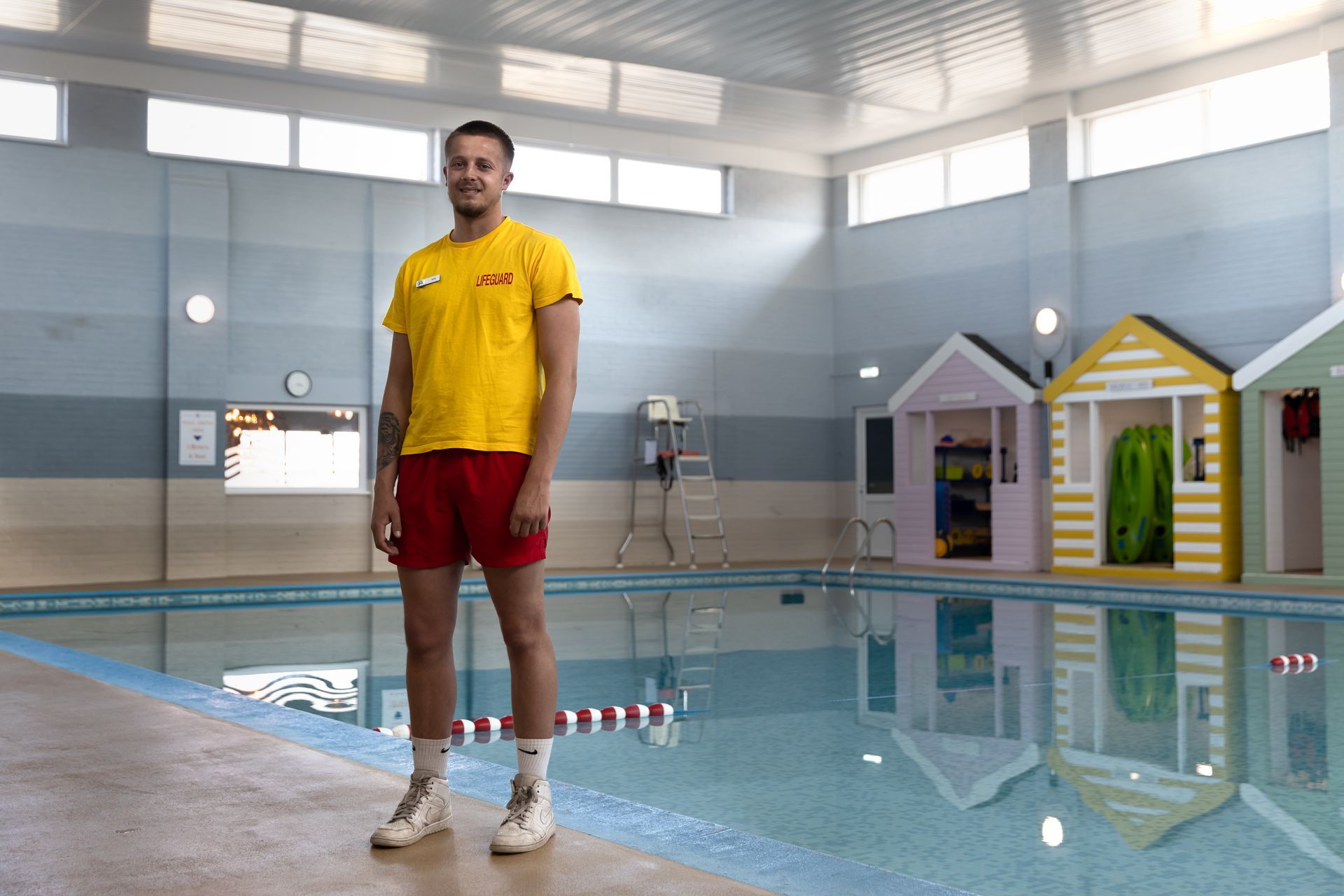 A man in a yellow shirt and red shorts is standing in front of a swimming pool.