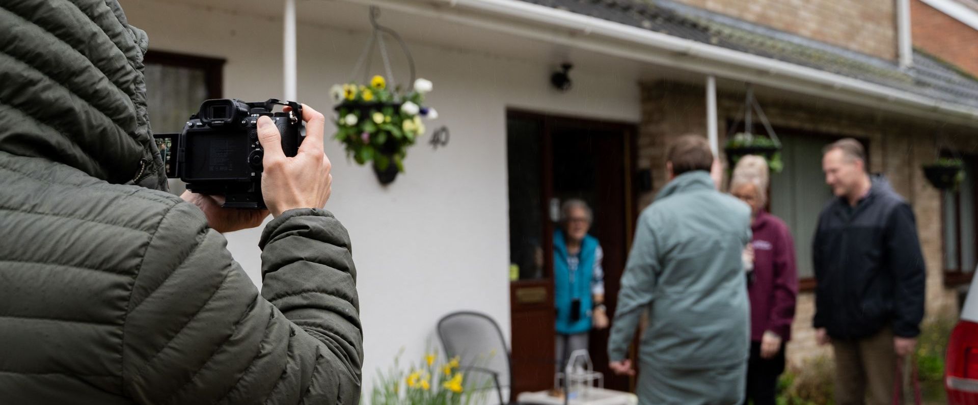 A man is taking a picture of a group of people standing outside of a house.
