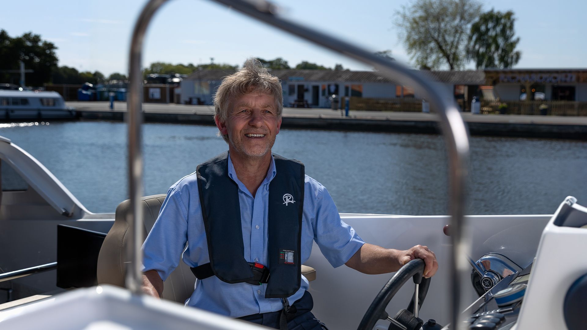 A man is sitting at the steering wheel of a boat.