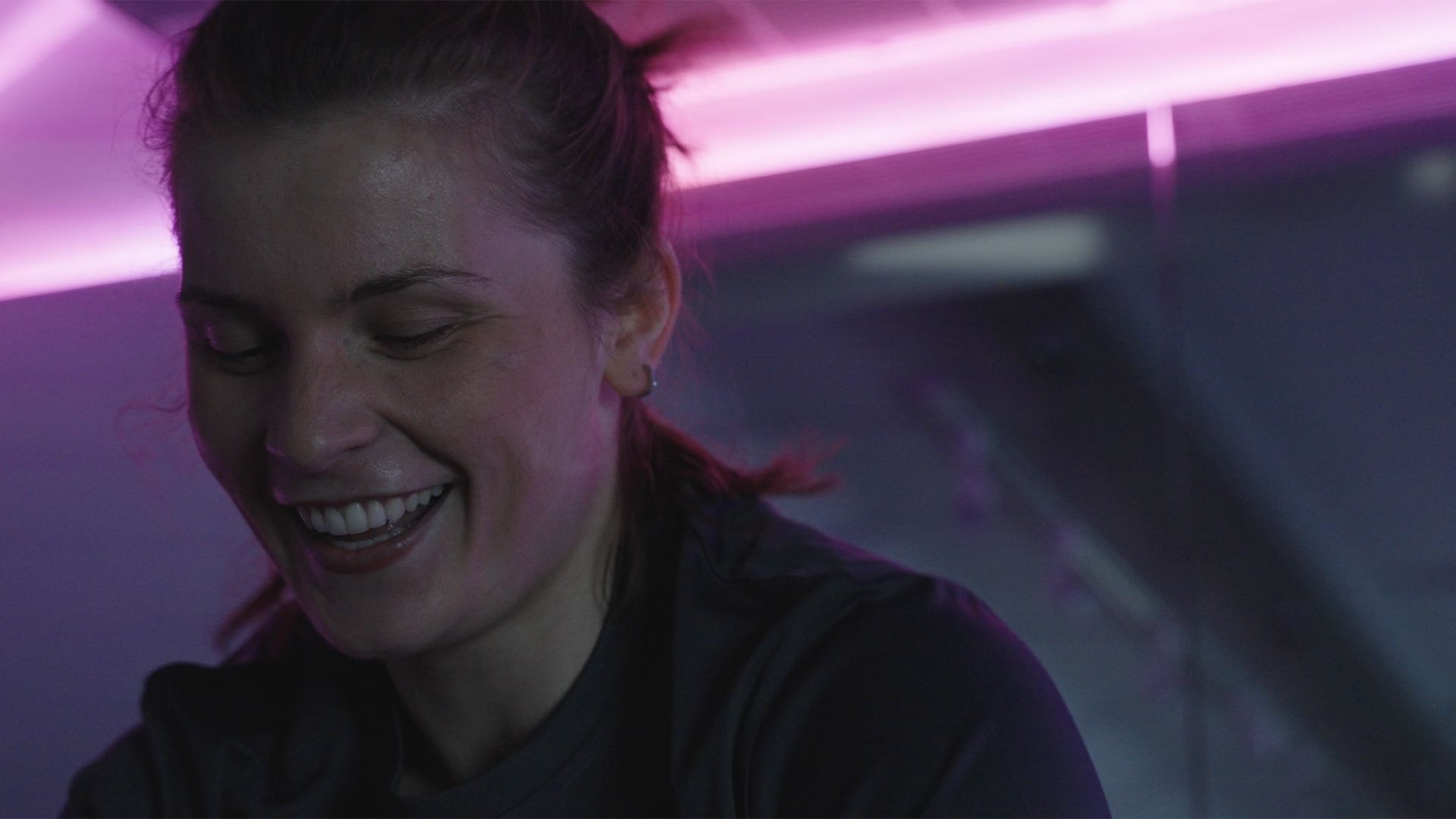 A woman is smiling while sitting on a bicycle in a dark room.