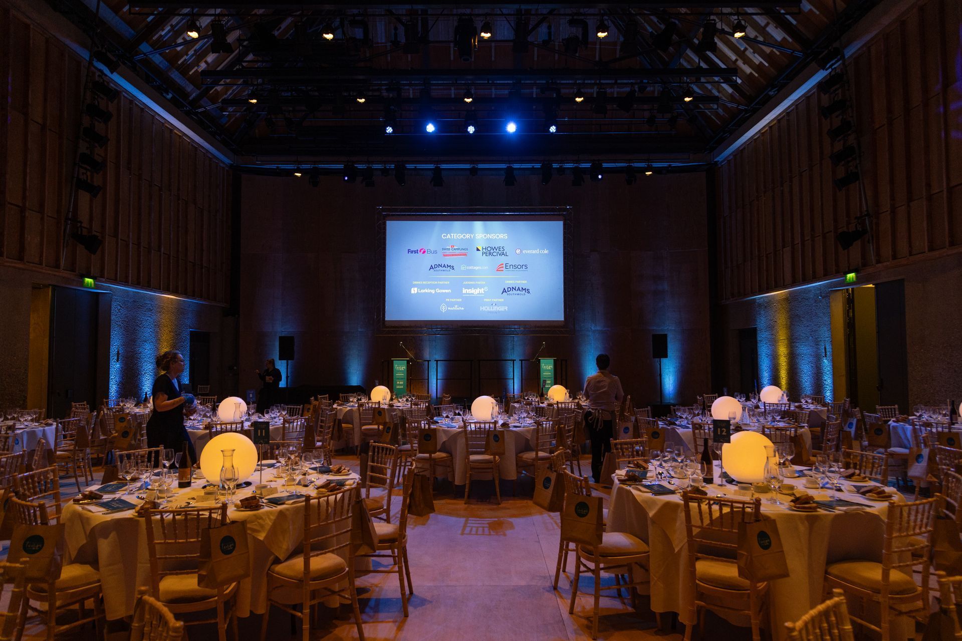 A large room with tables and chairs and a large screen on the wall.