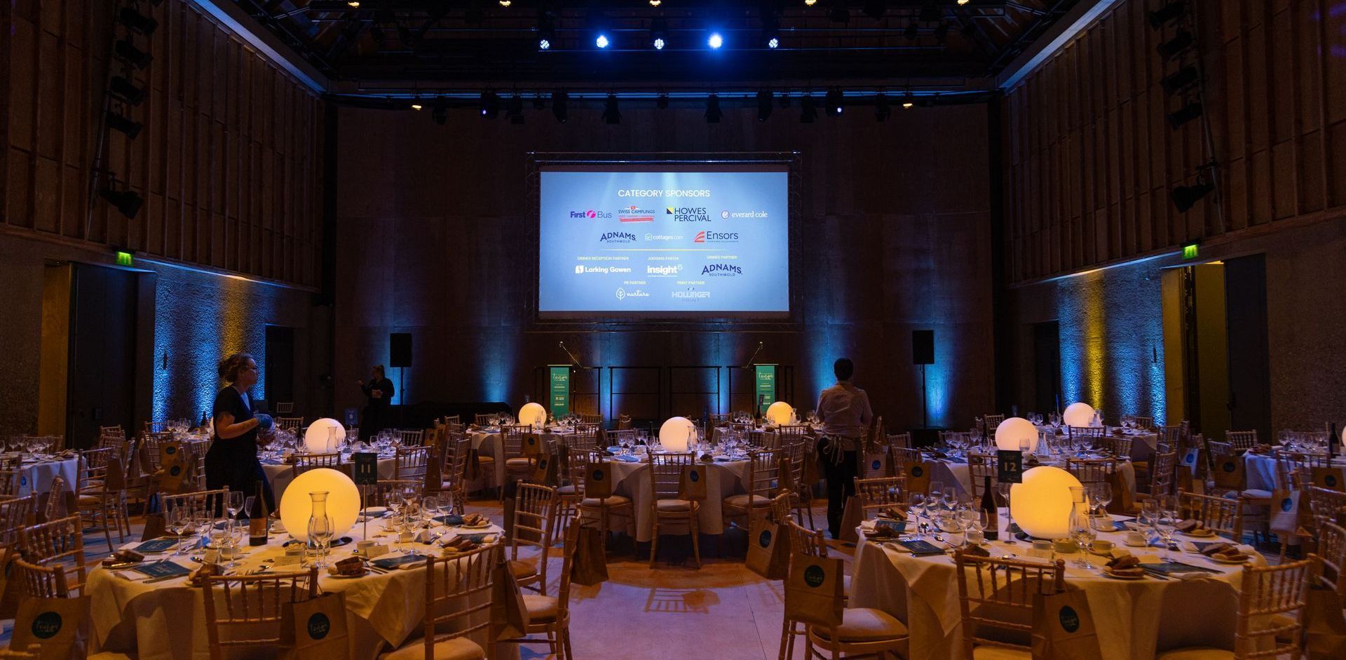 A large room filled with tables and chairs and a large screen.