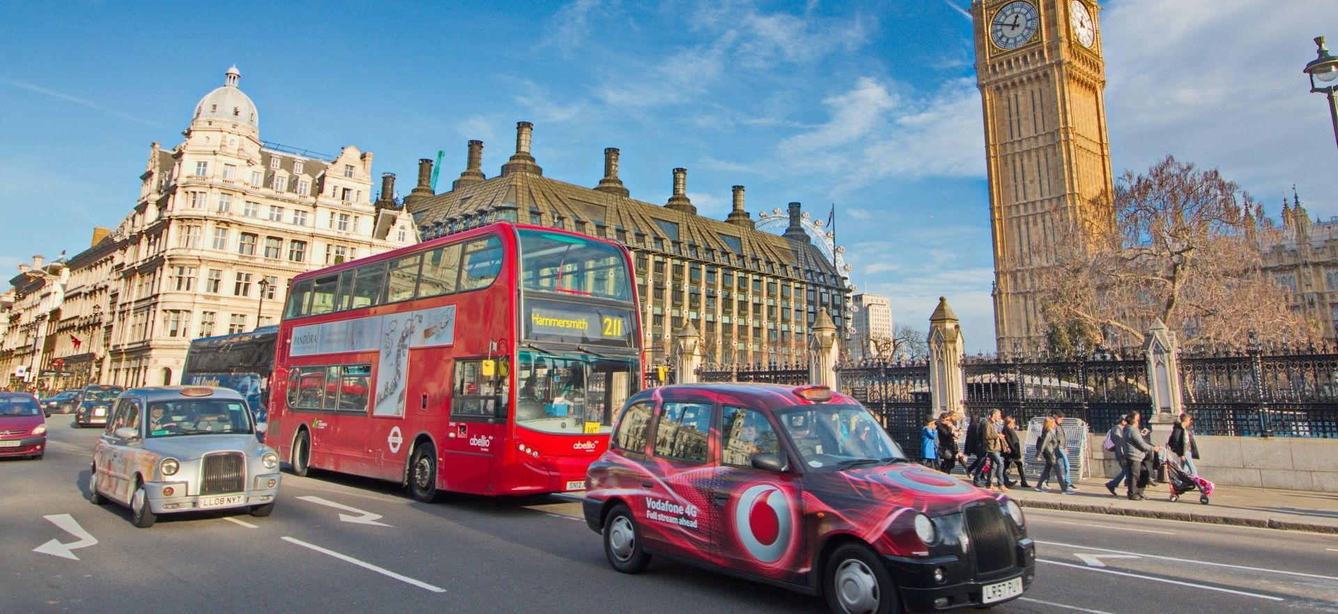A red double decker bus and a red taxi are driving down a street in london.