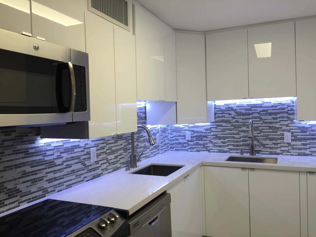 Modern white kitchen with gray mosaic backsplash, black appliances, and under-cabinet lighting