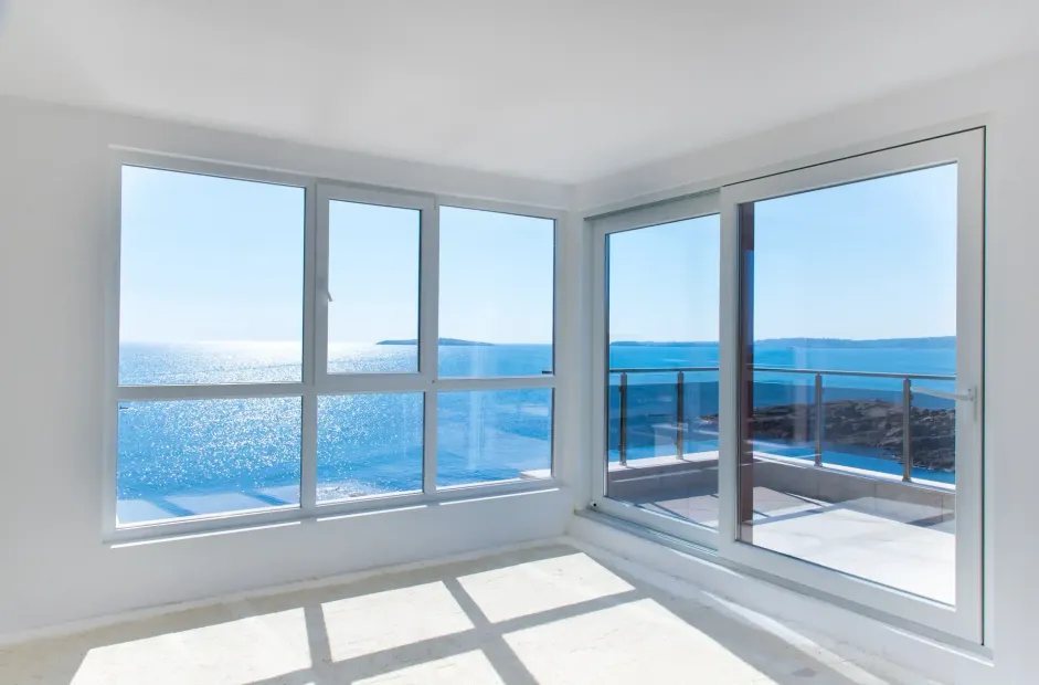 Bright empty room with large windows overlooking a blue ocean and sunny balcony.