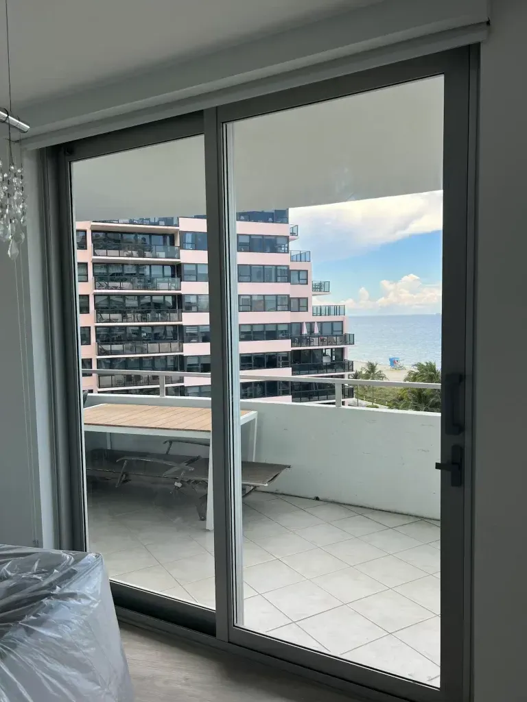 Sliding glass doors open to a balcony with a city view and distant ocean.