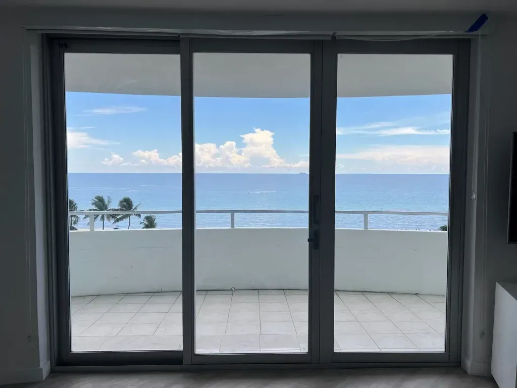 Sliding glass doors open to a balcony with ocean view and blue sky.