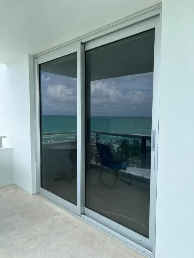 Sliding glass doors reflecting a balcony and ocean view at sunset