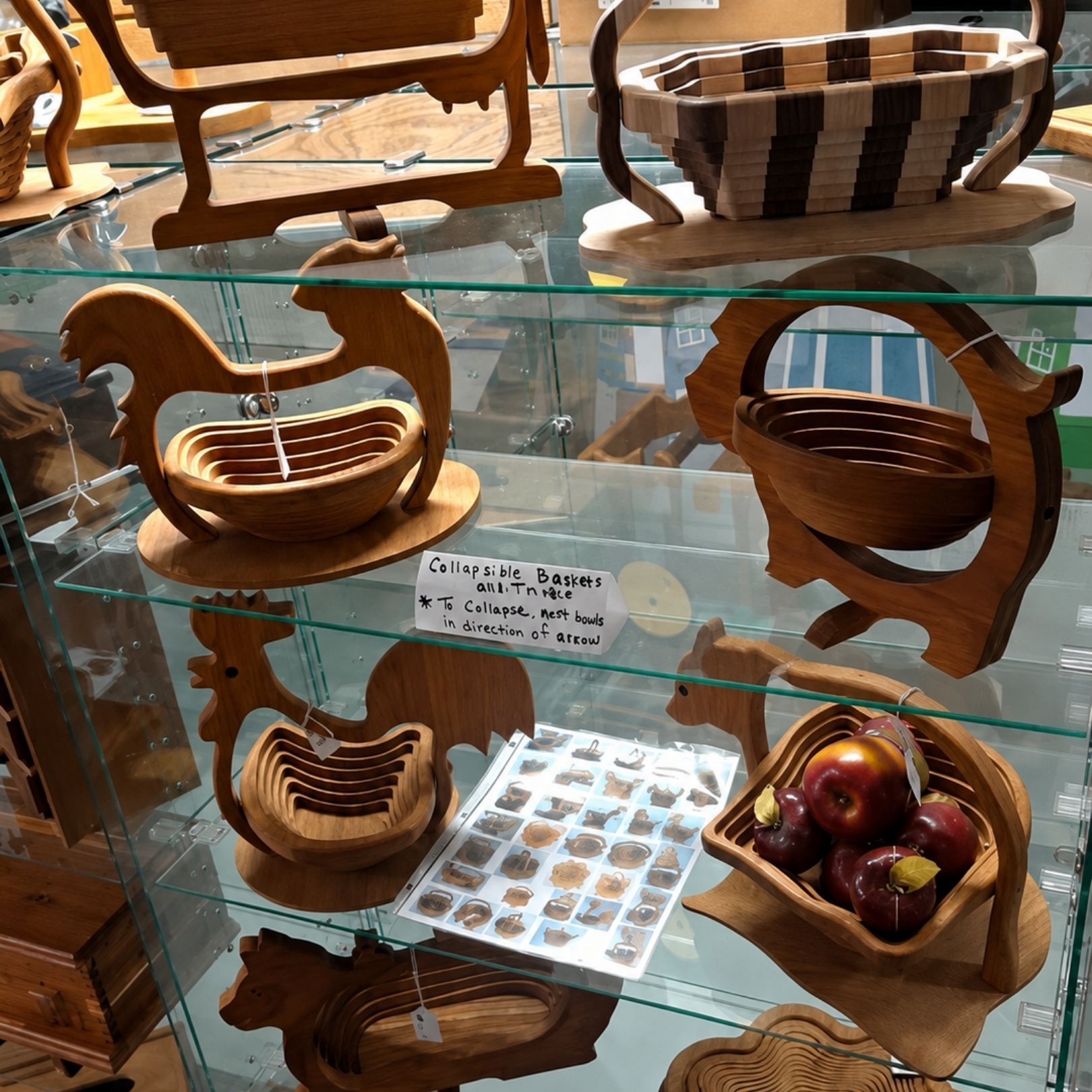 Glass display shelf with carved wooden baskets and a bowl of apples in a shop window