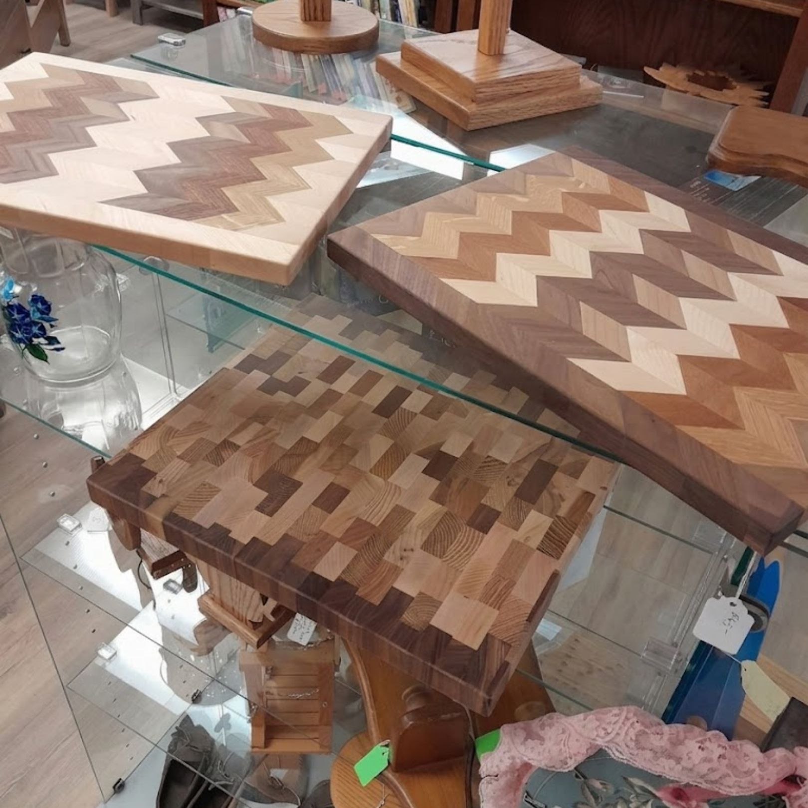 Wooden cutting boards and serving trays displayed on a glass shelf in a shop