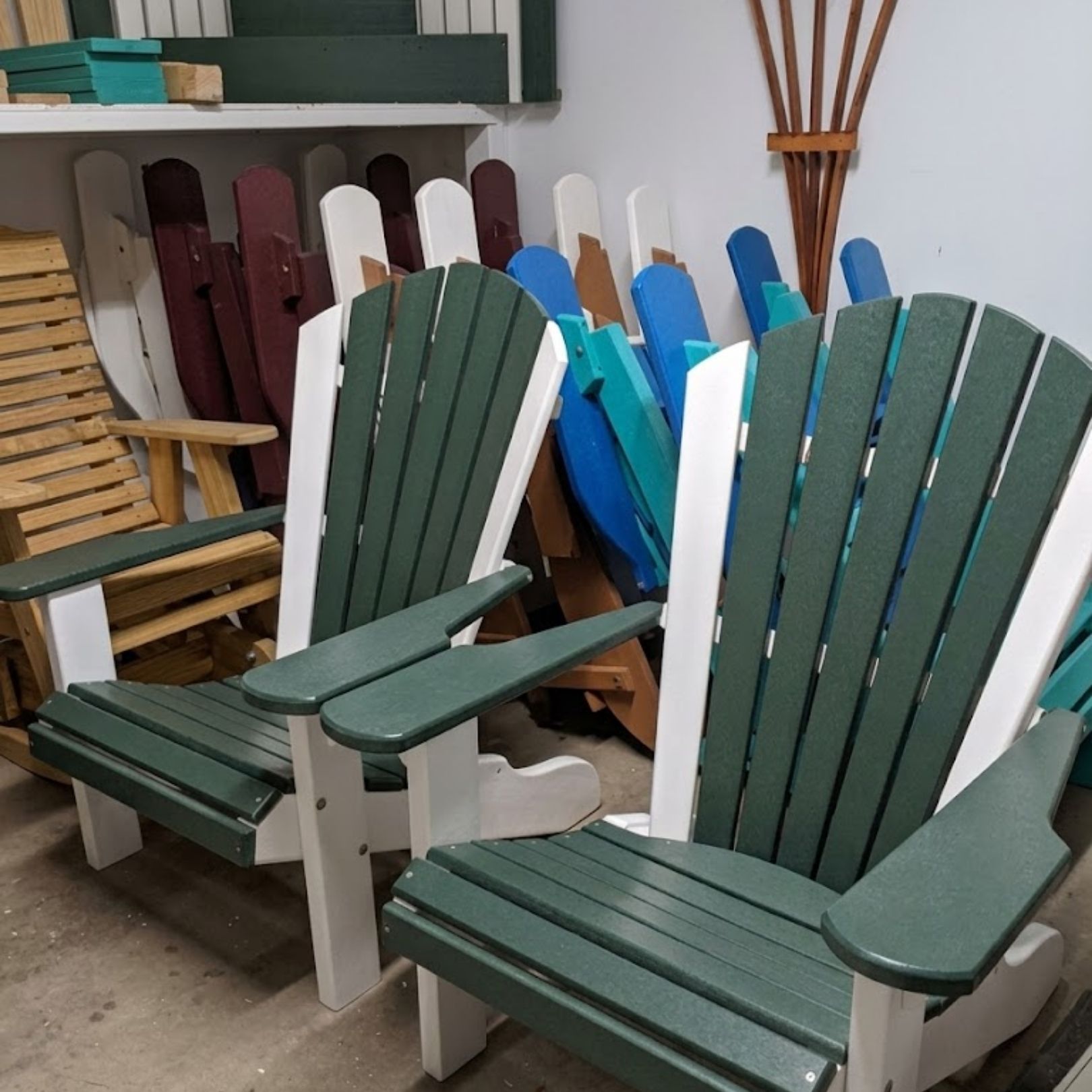 Green Adirondack chairs displayed in a workshop, surrounded by unfinished wooden chairs and decor pieces
