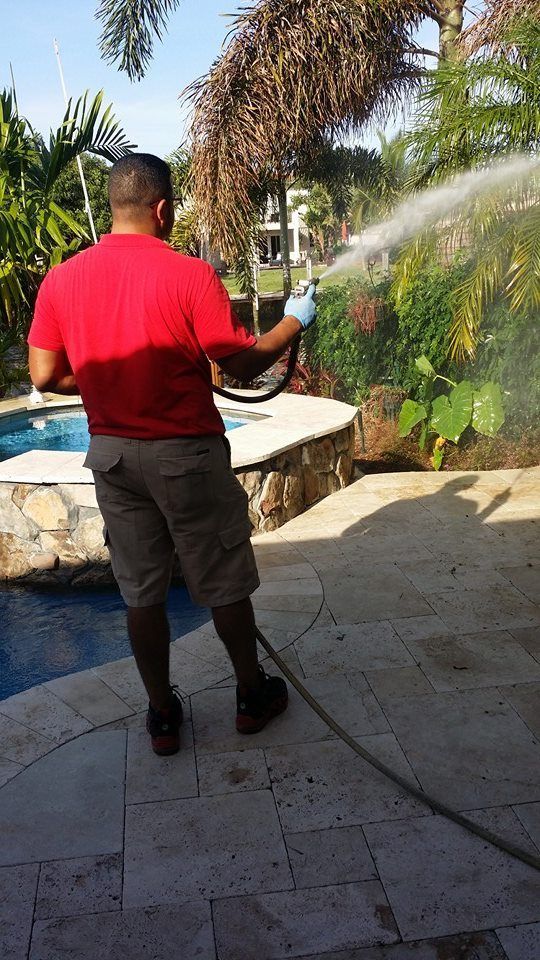 A man is spraying water from a hose on a patio.