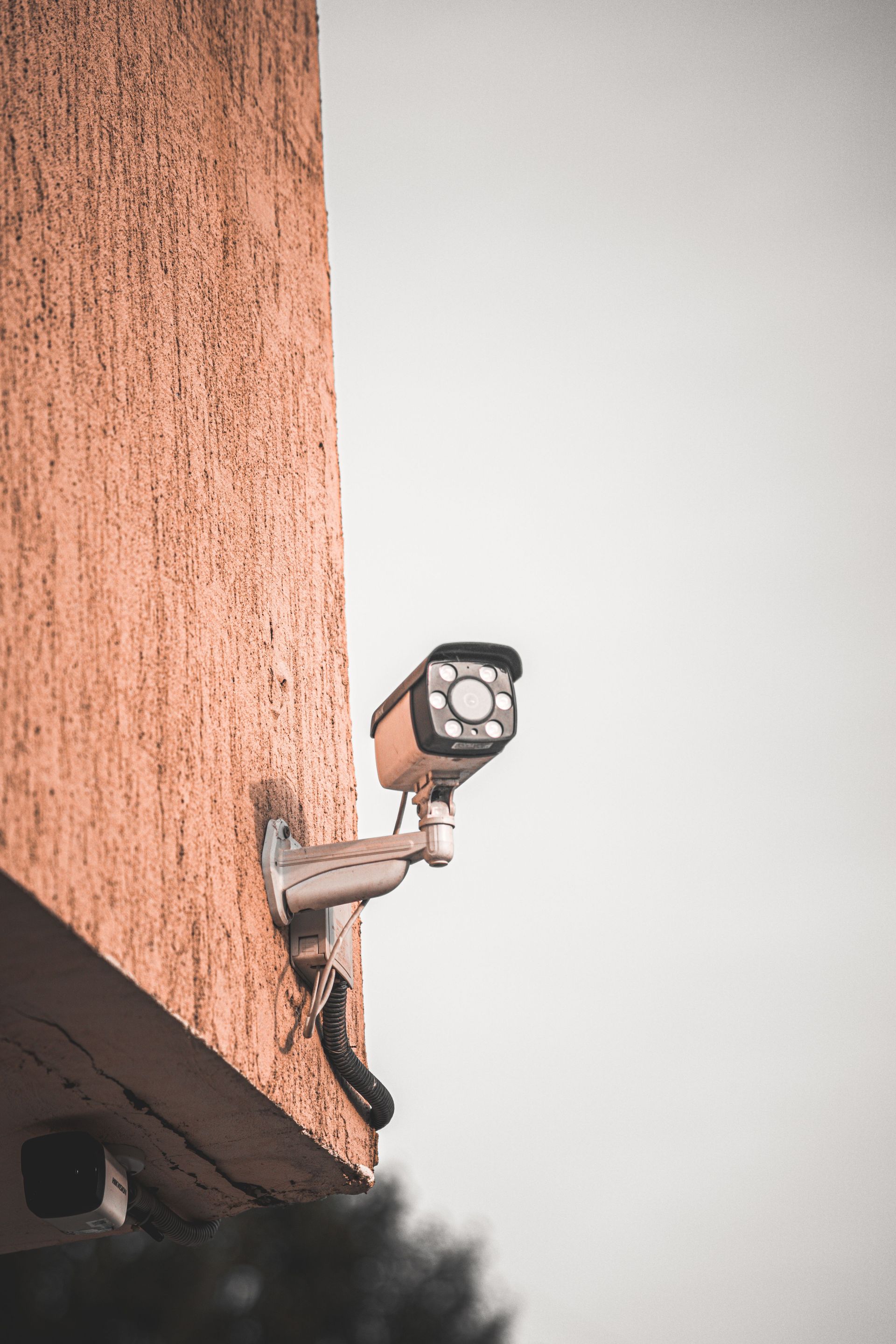 Security camera mounted on a building corner, angled outward against a pale sky.
