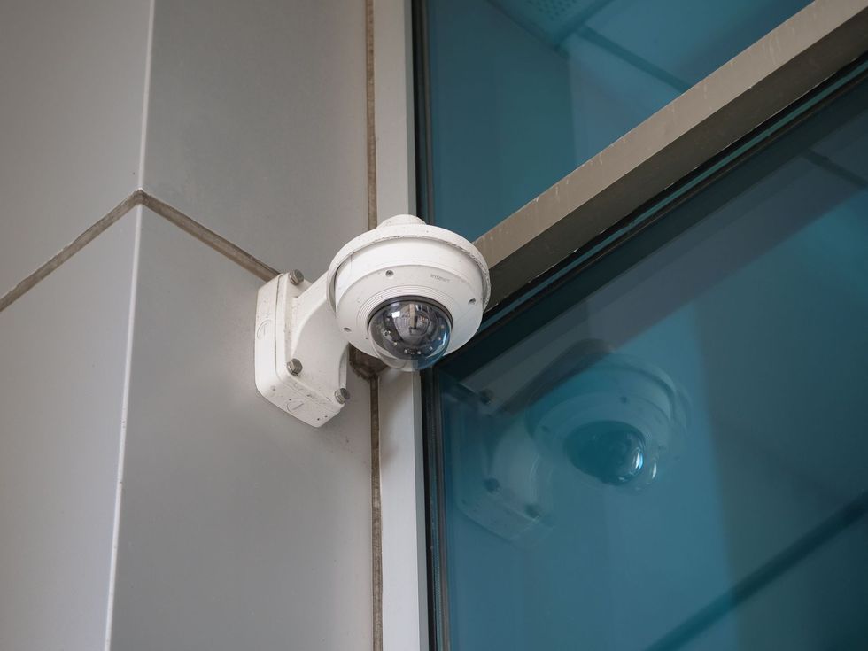 Wall-mounted security camera beside a blue-tinted glass building corner.