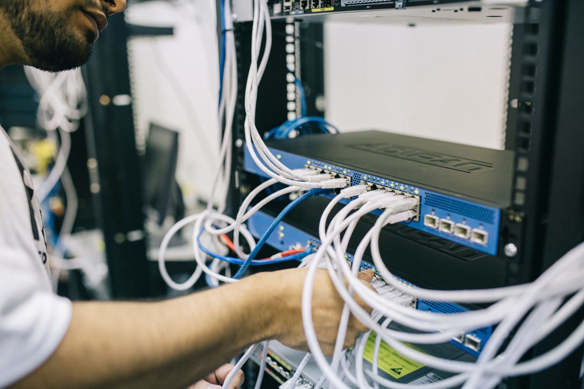 Technician organizing cables inside a network server rack with a blue switch.