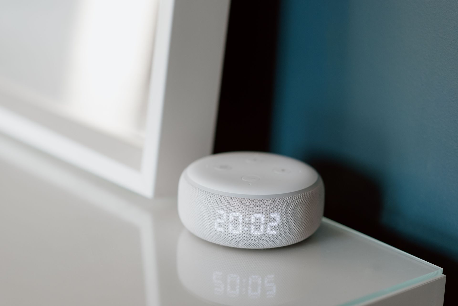 White smart speaker with digital display on a glossy table near a window