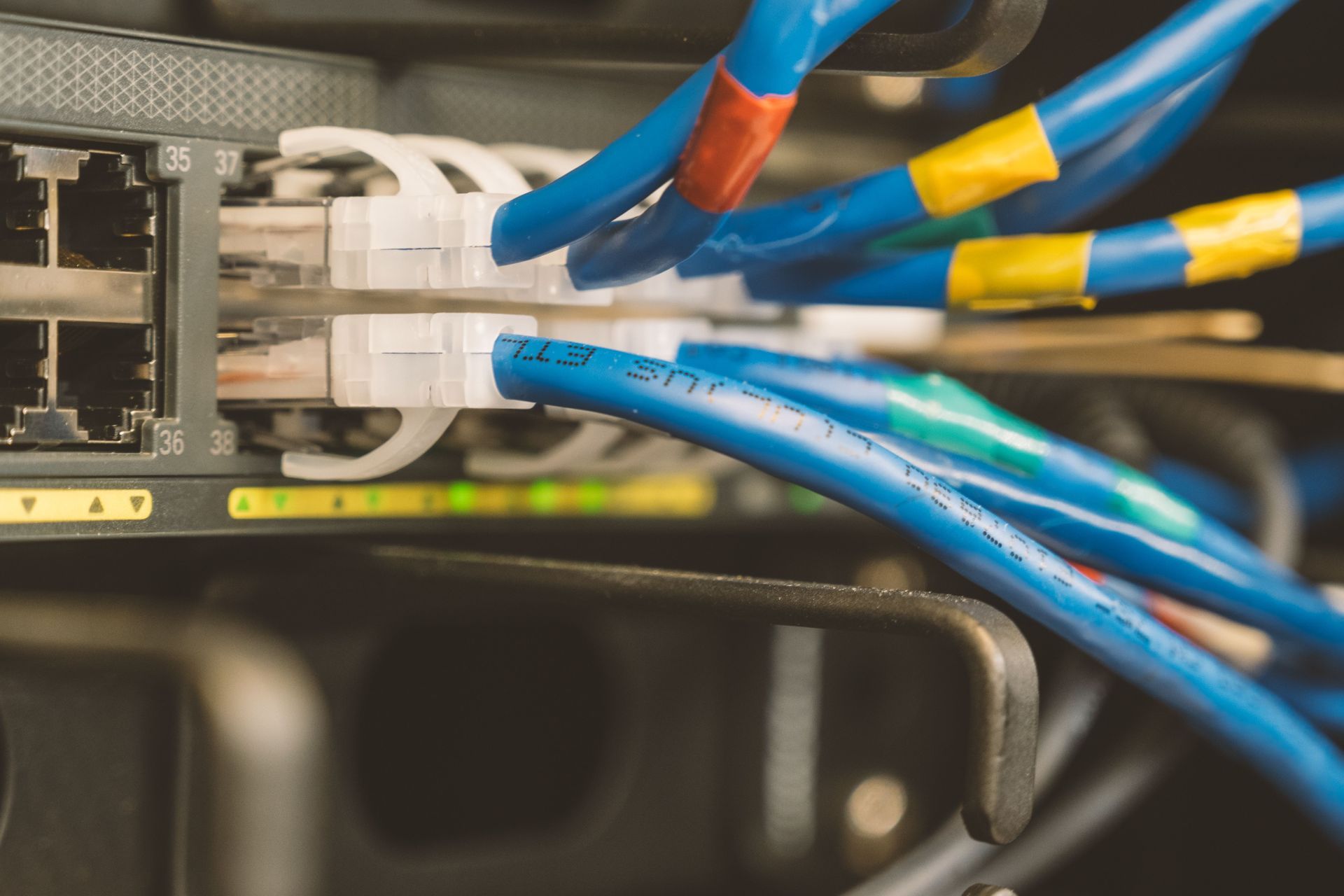 Close-up of network cables plugged into a switch, with blue and yellow wires in a server rack.