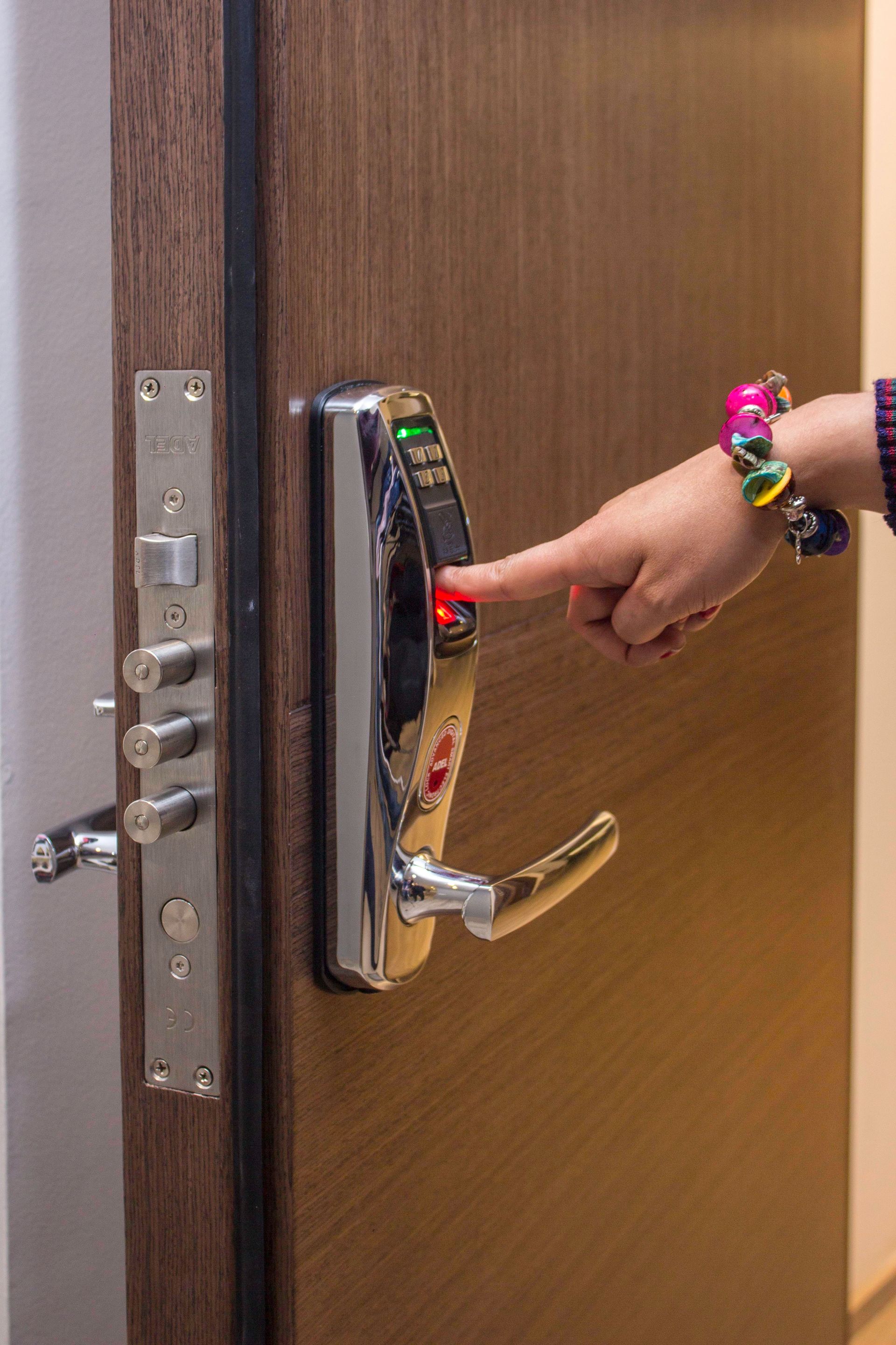 Hand pressing a red button on a door lock keypad, with a wooden door open slightly