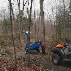 Une déchiqueteuse à bois bleue est garée au milieu d'une forêt à côté d'un quatre roues.