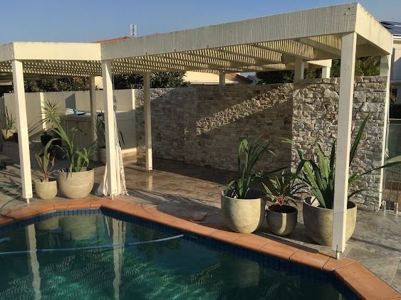 A Swimming Pool With A Pergola And Potted Plants Around It — Green Envy Landscapes Pty Ltd In Carrara, QLD