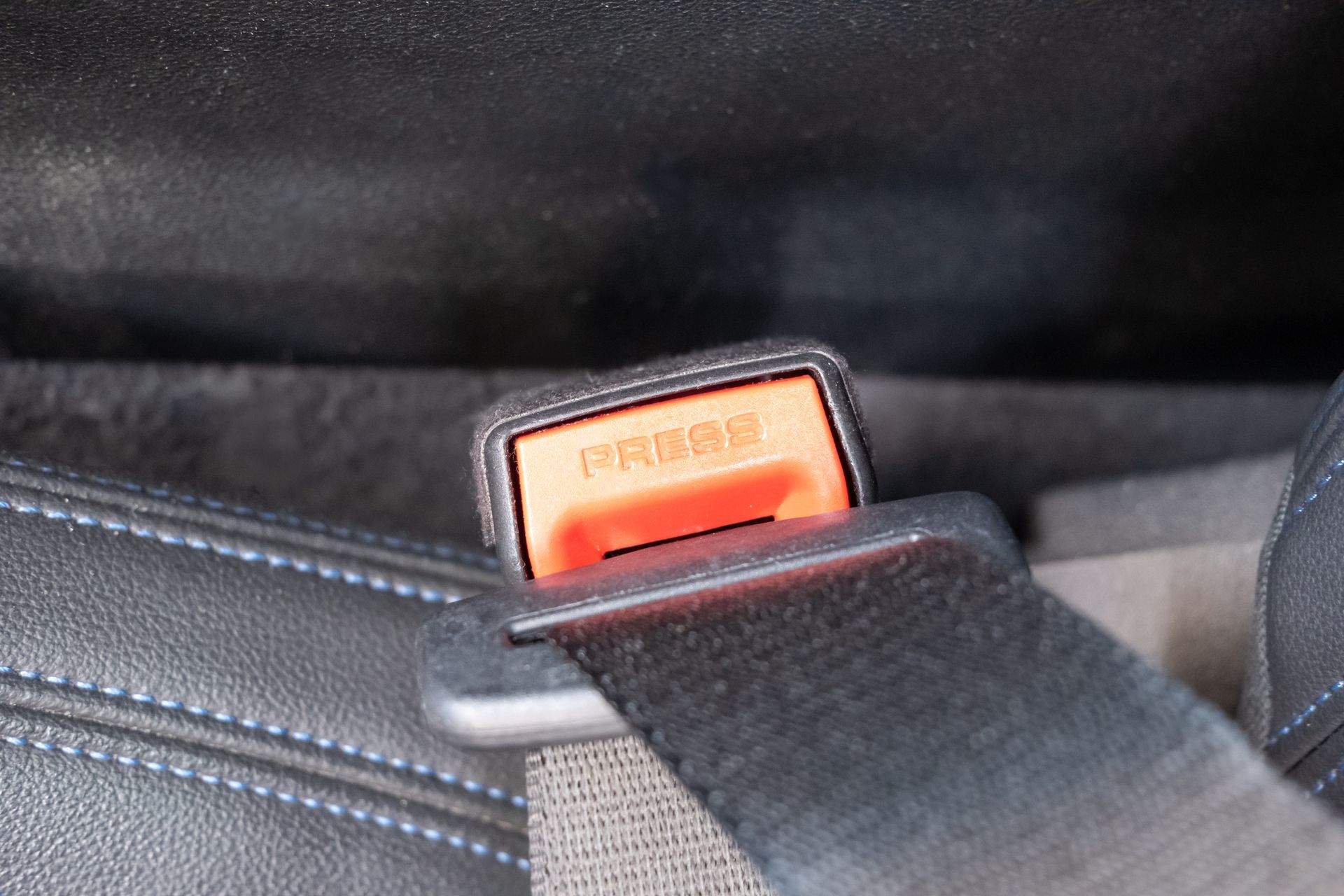A close-up of a black seatbelt fastened into an orange release buckle with the word 