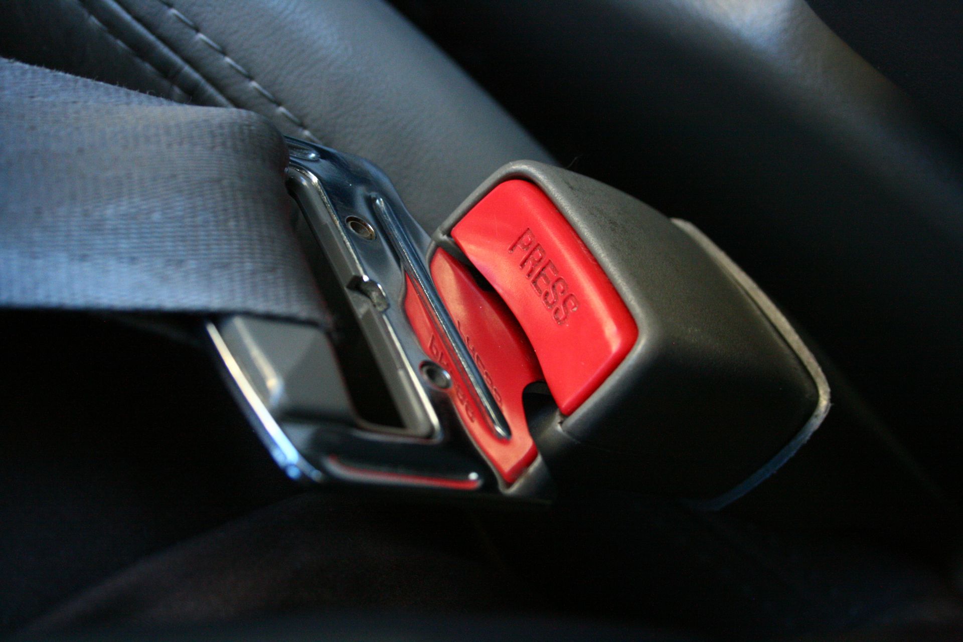 A fastened black car seat belt with a red release button labeled 