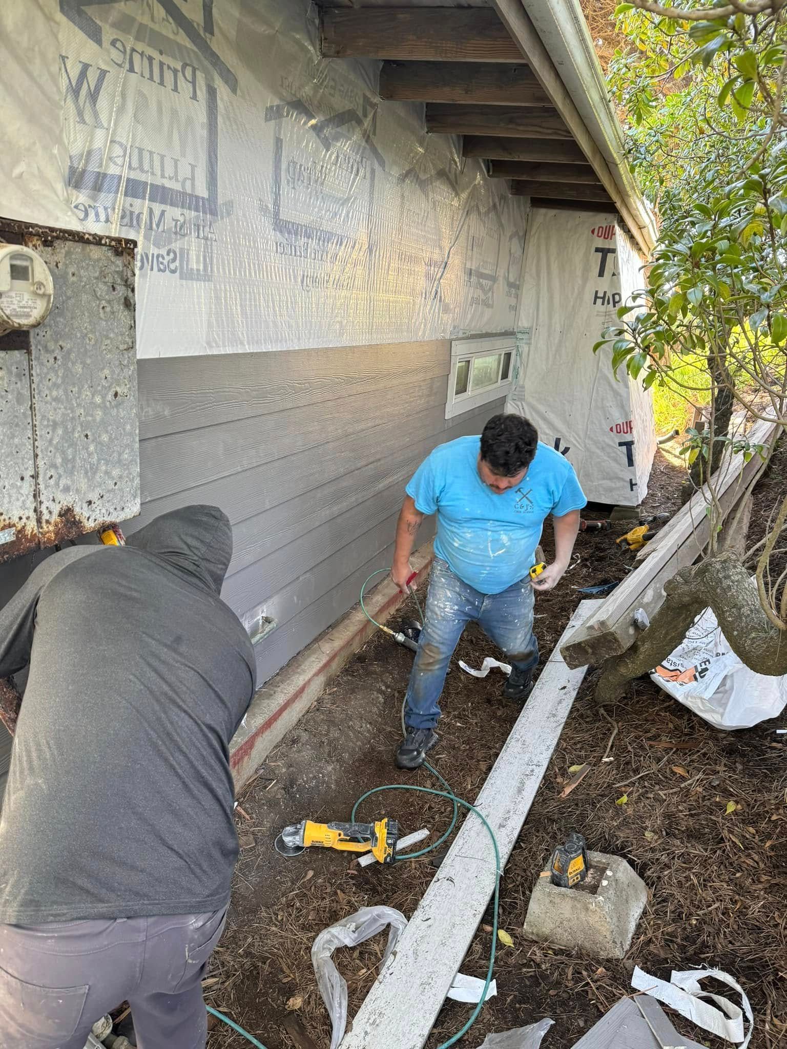 Two men installing siding on a building exterior. One in blue shirt, the other in gray hoodie.