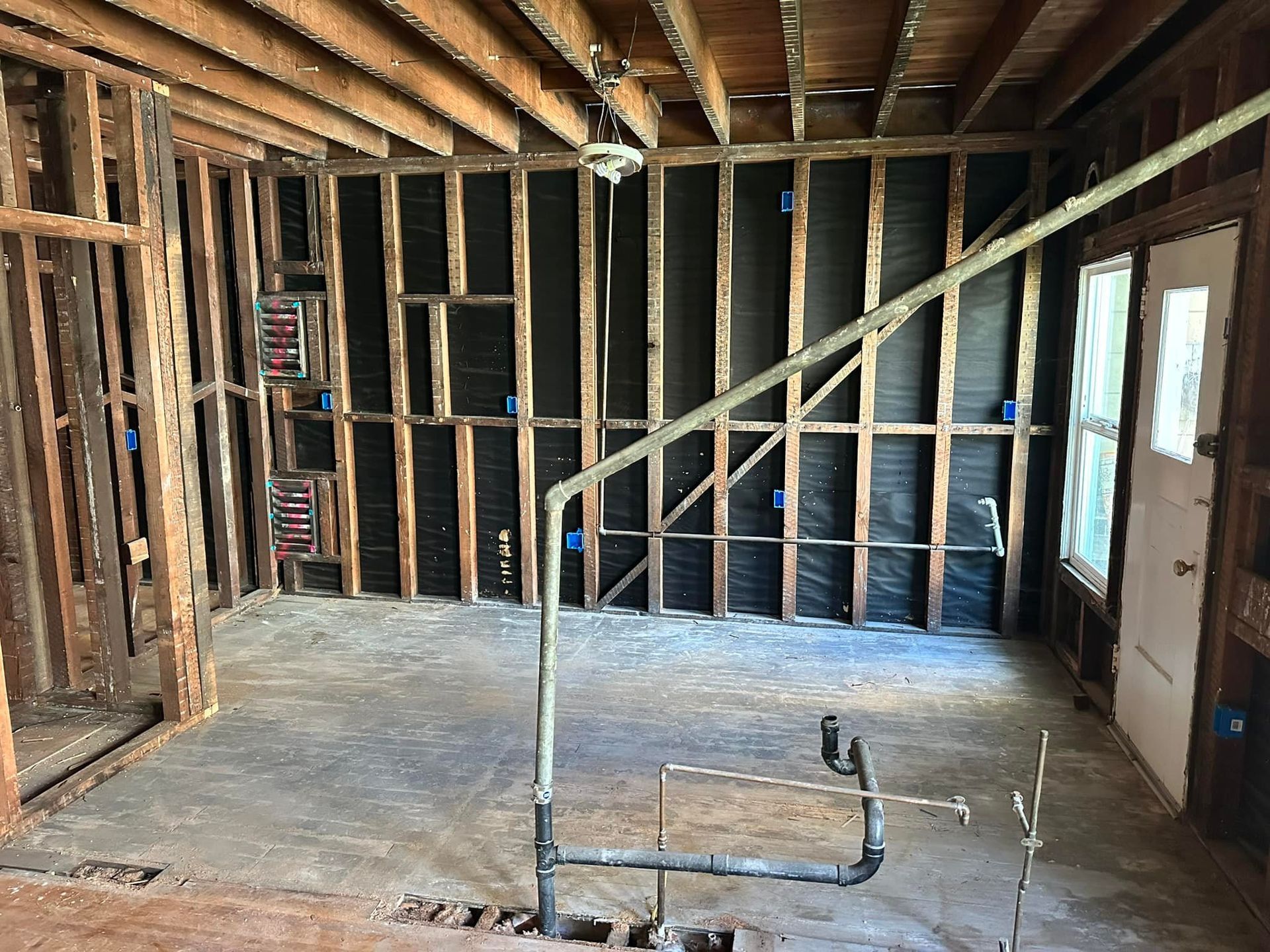 Interior of a room under renovation: exposed studs, plumbing, wiring, and door.
