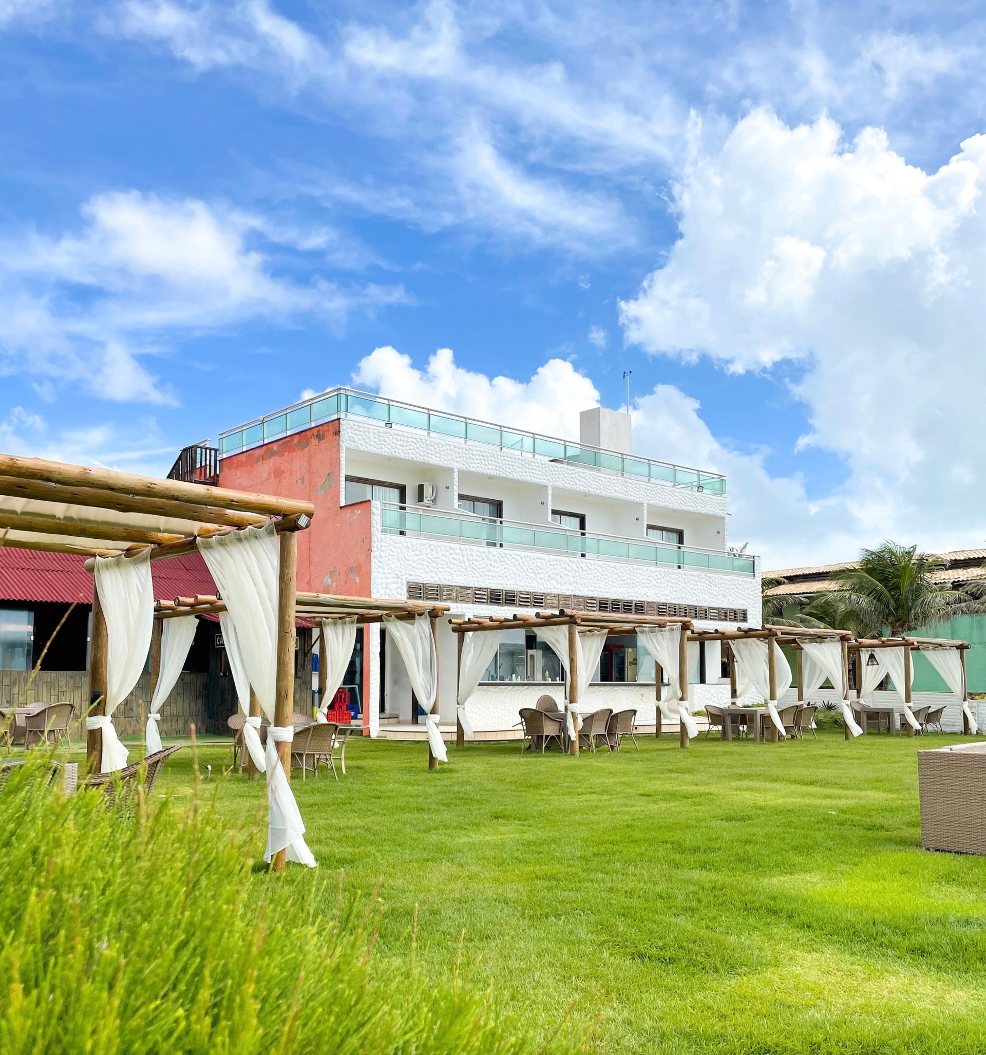 Prédio branco com área de estar coberta em gramado verde sob céu azul.