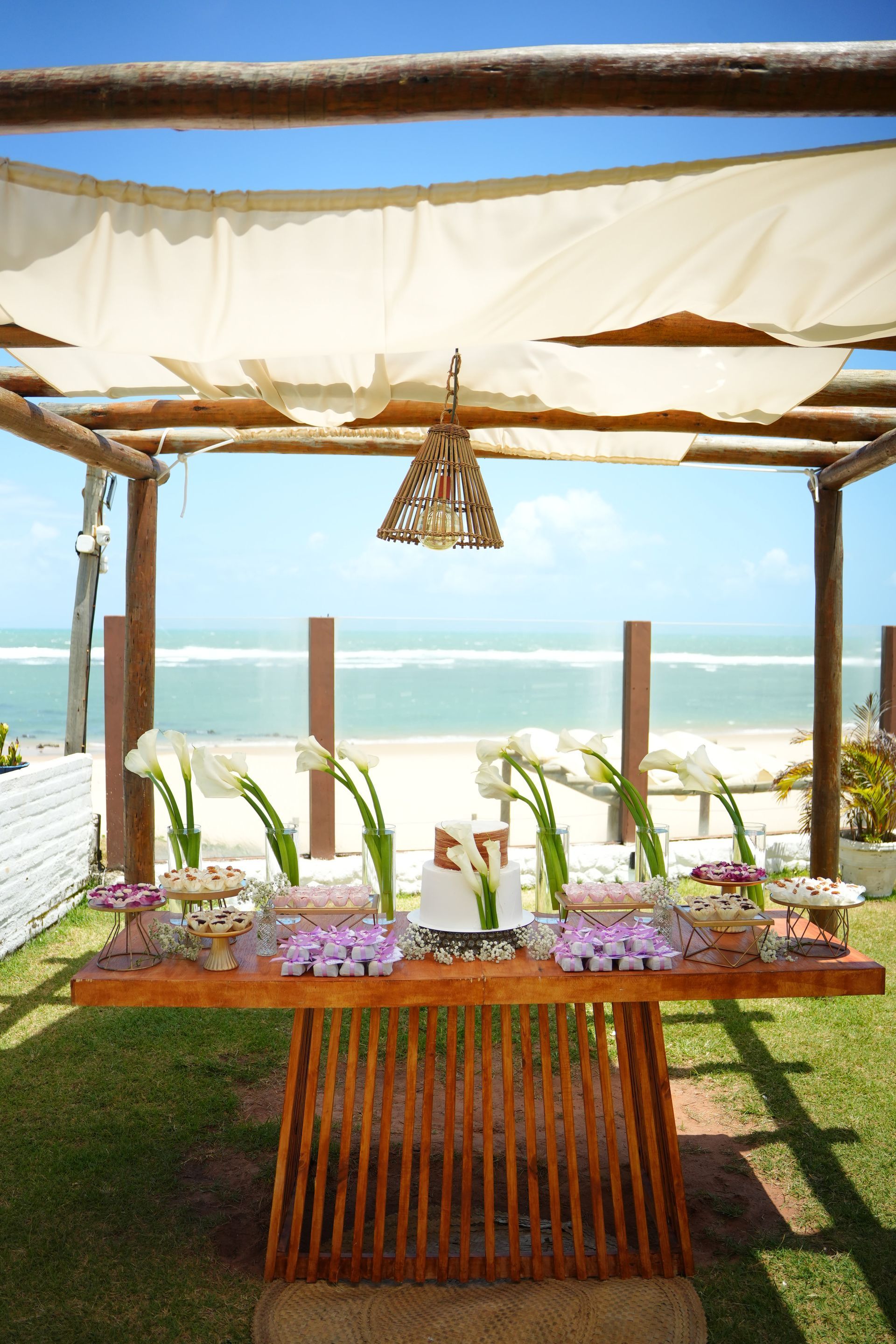 Mesa de sobremesas com doces sob um toldo, com vista para a praia.