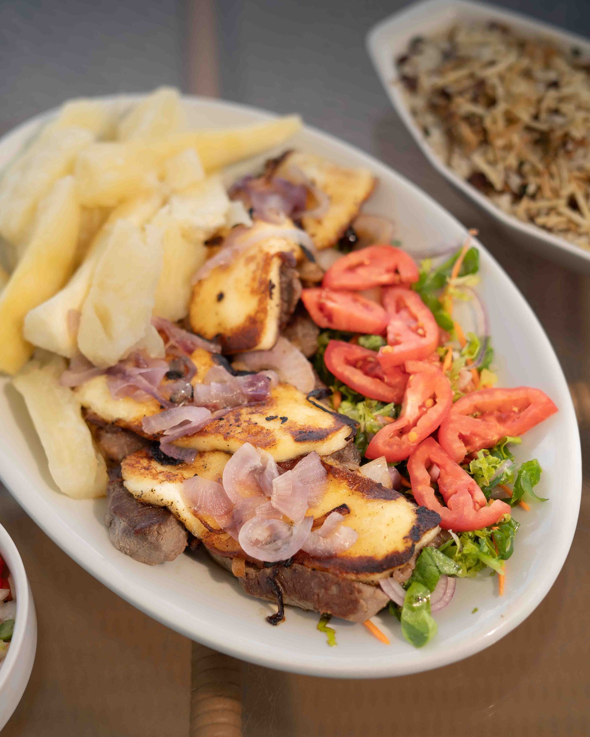 Prato de queijo halloumi grelhado com tomates, cebolas, salada e mandioca.