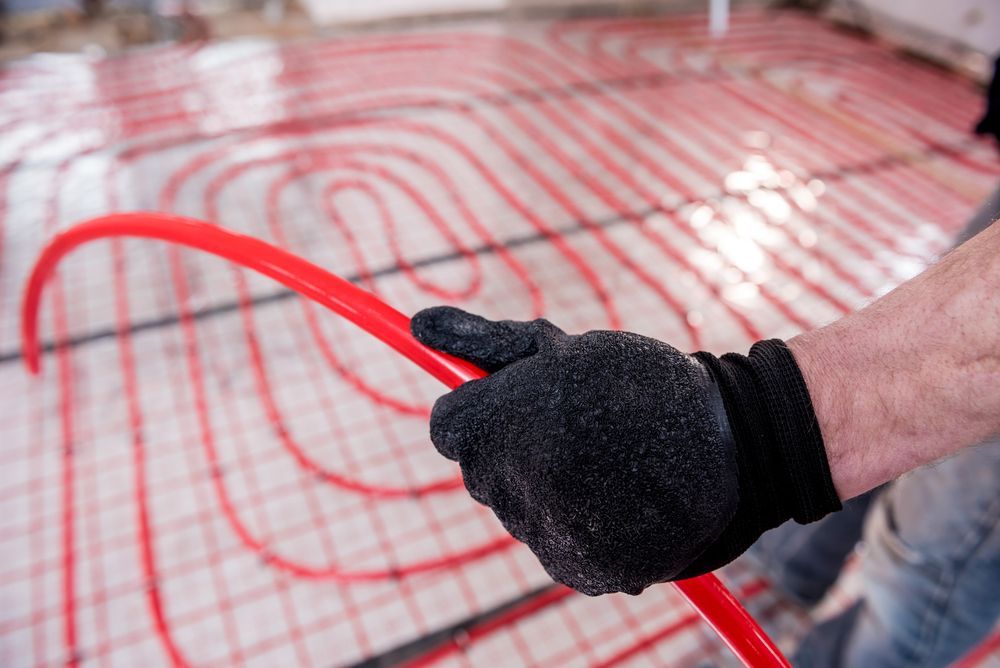 Person Wearing Gloves Holding a Red Radiant Floor Heating Tube — Illawarra Underfloor Heating In Bellambi, NSW