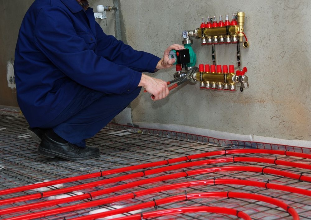 A Person Uses Pliers on Plumbing Connected to Red Tubing — Illawarra Underfloor Heating In Ulladulla, NSW