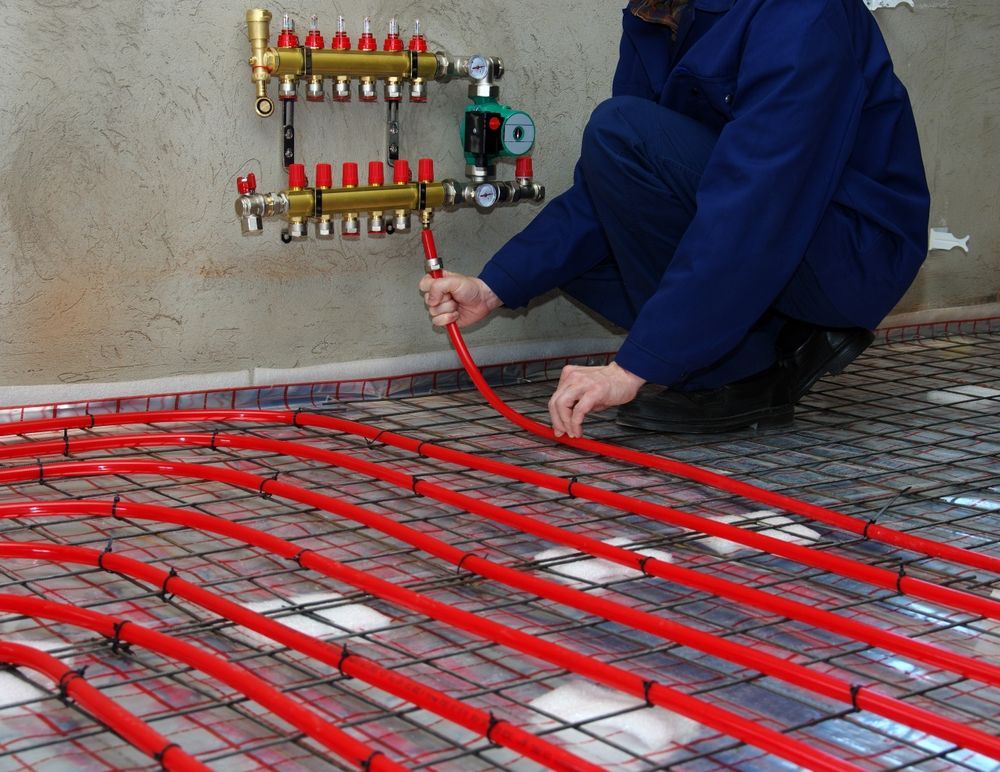 Person Connecting Red Tubing to Manifold — Illawarra Underfloor Heating In Kiama, NSW