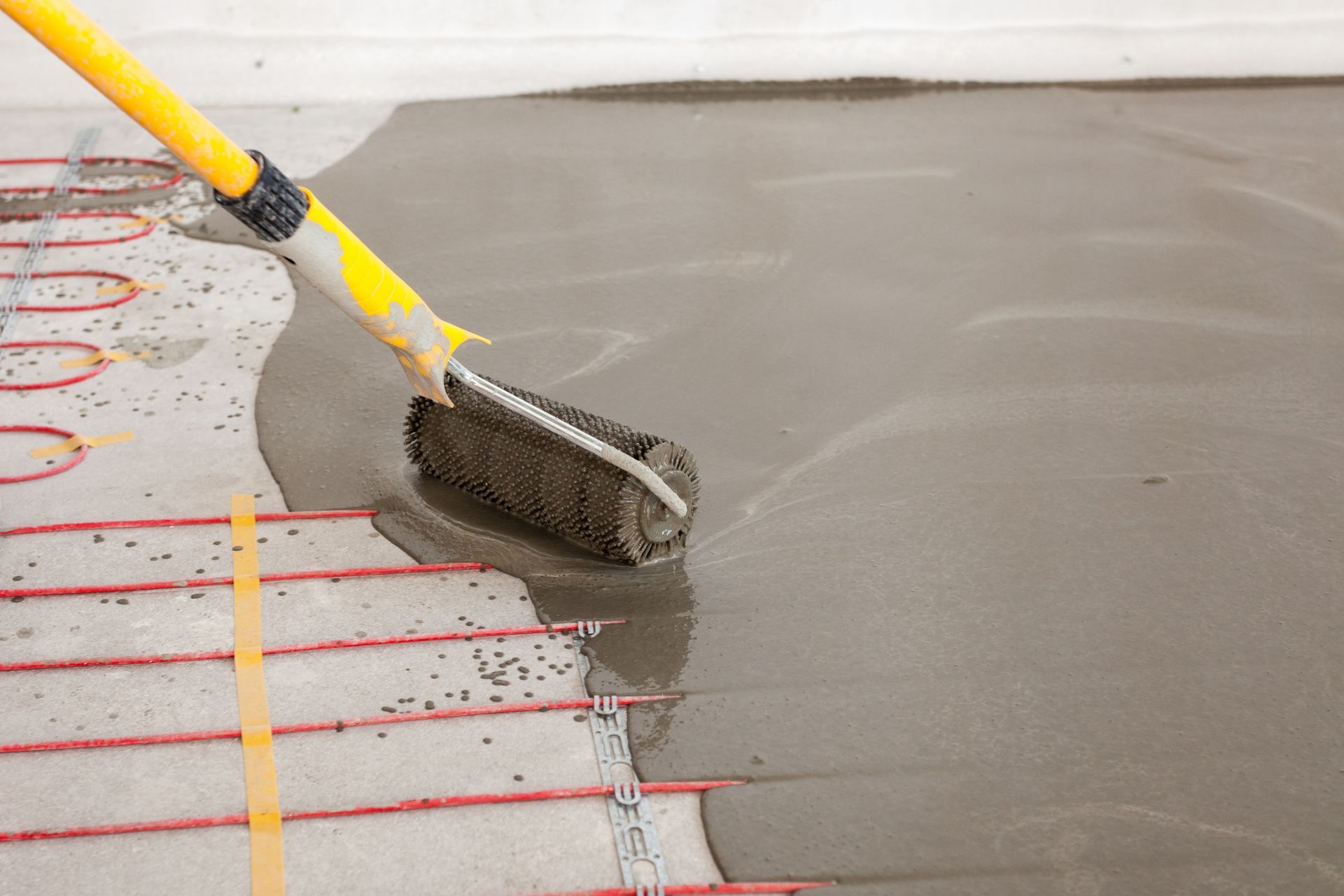 A Person Is Applying a Self-Leveling Concrete Floor with A Roller — Illawarra Underfloor Heating In Shellharbour, NSW