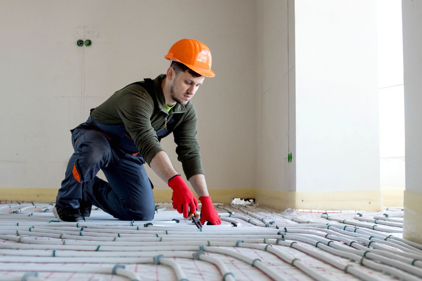 Construction Worker Kneeling and Cutting Pipe  — Illawarra Underfloor Heating In Kiama, NSW