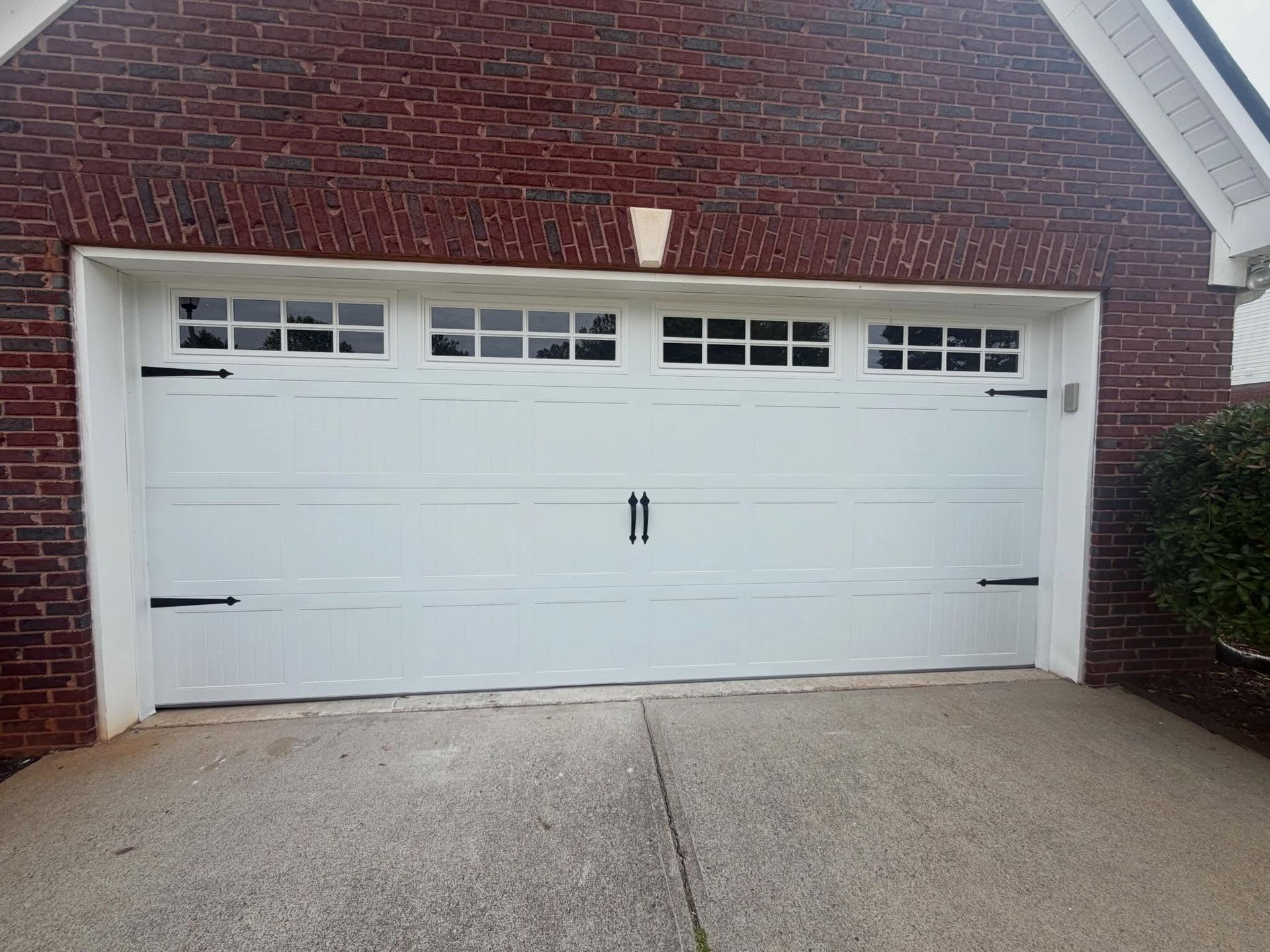 White double garage door on a brick house with a concrete driveway and small shrubs.