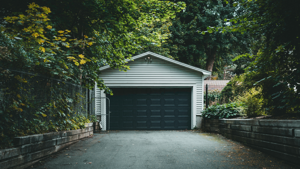 Detached garage at the end of a tree-lined driveway, with a white exterior and dark garage door.