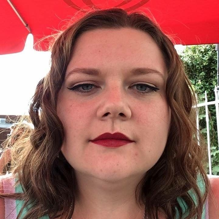 A woman with red lipstick is sitting under a red umbrella