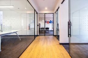 Modern office hallway with glass-walled meeting rooms and a wood floor