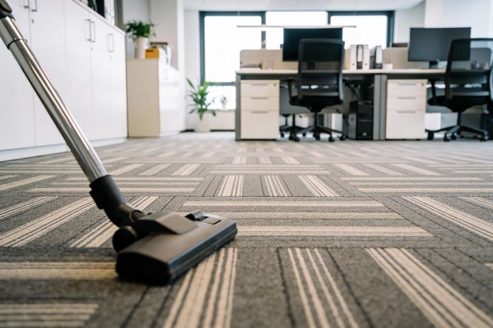 Vacuum cleaner head on patterned office carpet with desks and chairs in the background