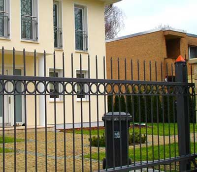 Frente a una casa hay una valla de hierro forjado.
